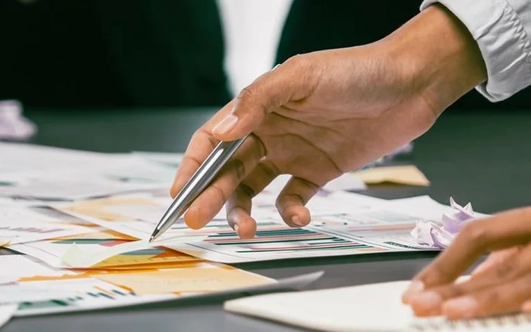 a hand holding a pen over papers
