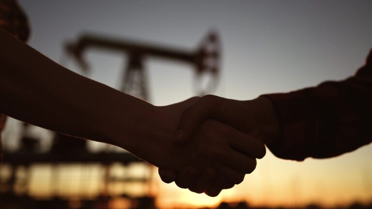 two persons shaking hands against the backdrop of an oil pump